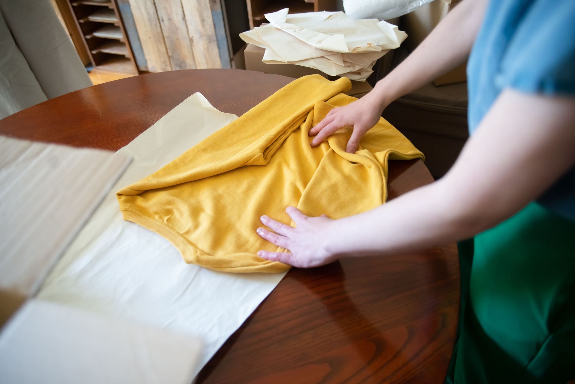Hands folding a yellow shirt on a wooden table, showcasing a clothing chore indoors.